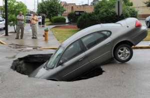 Image Credit: AP A car rests in a hole after a water main broke on Oregon St. at Main St. in Evansville, Ind. on Friday, May 30, 2014. The car's owner, rear left, said he, his girlfriend and two children were in the car at the time.